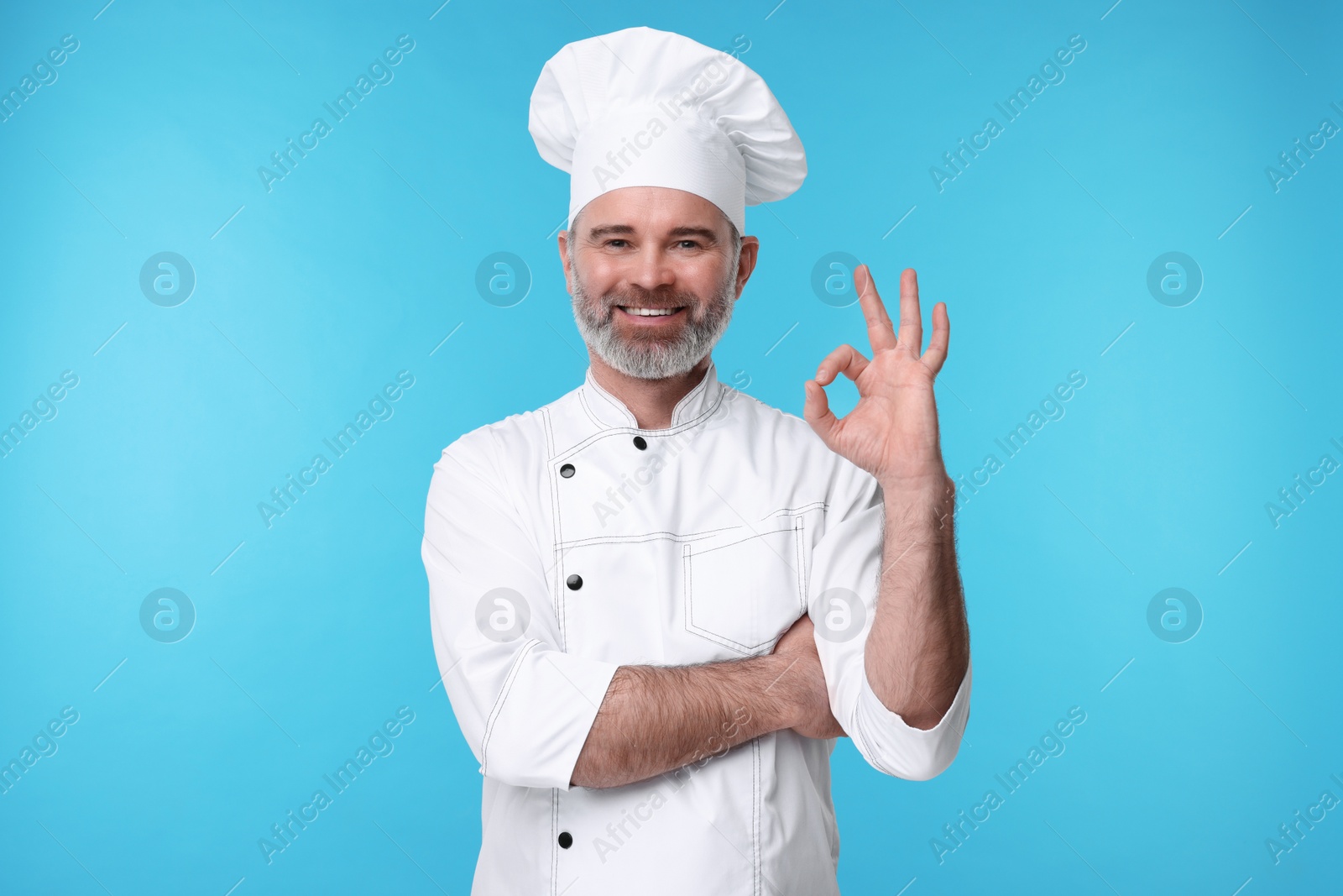 Photo of Happy chef in uniform showing OK gesture on light blue background