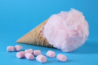 Photo of Sweet cotton candy in waffle cone and marshmallows on light blue background, closeup