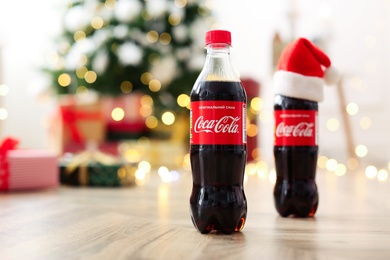 Photo of MYKOLAIV, UKRAINE - January 01, 2021: Bottles of Coca-Cola on floor against blurred Christmas lights