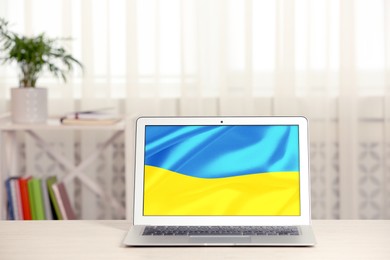Image of Modern laptop with picture of Ukrainian national flag on screen indoors