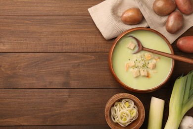 Photo of Bowl of tasty leek soup, spoon and ingredients on wooden table, flat lay. Space for text
