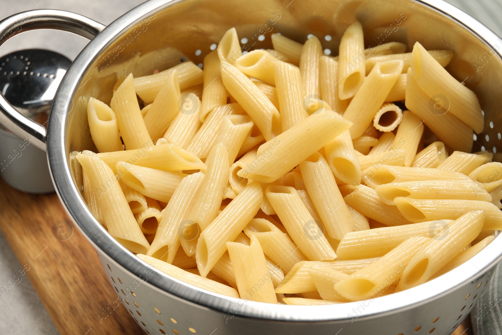 Photo of Delicious penne pasta in colander on table, closeup