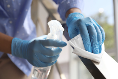 Photo of Woman in latex gloves cleaning railing with wet wipe and detergent indoors, closeup