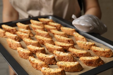 Photo of Woman holding baking tray with tasty cantucci indoors, closeup. Traditional Italian almond biscuits