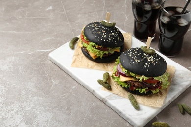 Photo of Board with black burgers and drinks on grey background, space for text