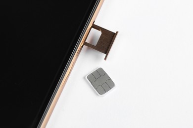 SIM card and mobile phone on white table, closeup