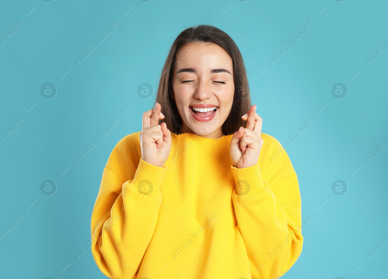 Photo of Woman with crossed fingers on light blue background. Superstition concept