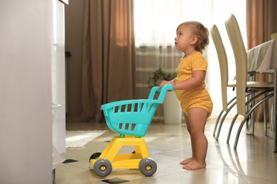 Cute baby with toy walker in room. Learning to walk