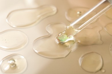 Photo of Dripping hydrophilic oil from pipette on beige background, closeup