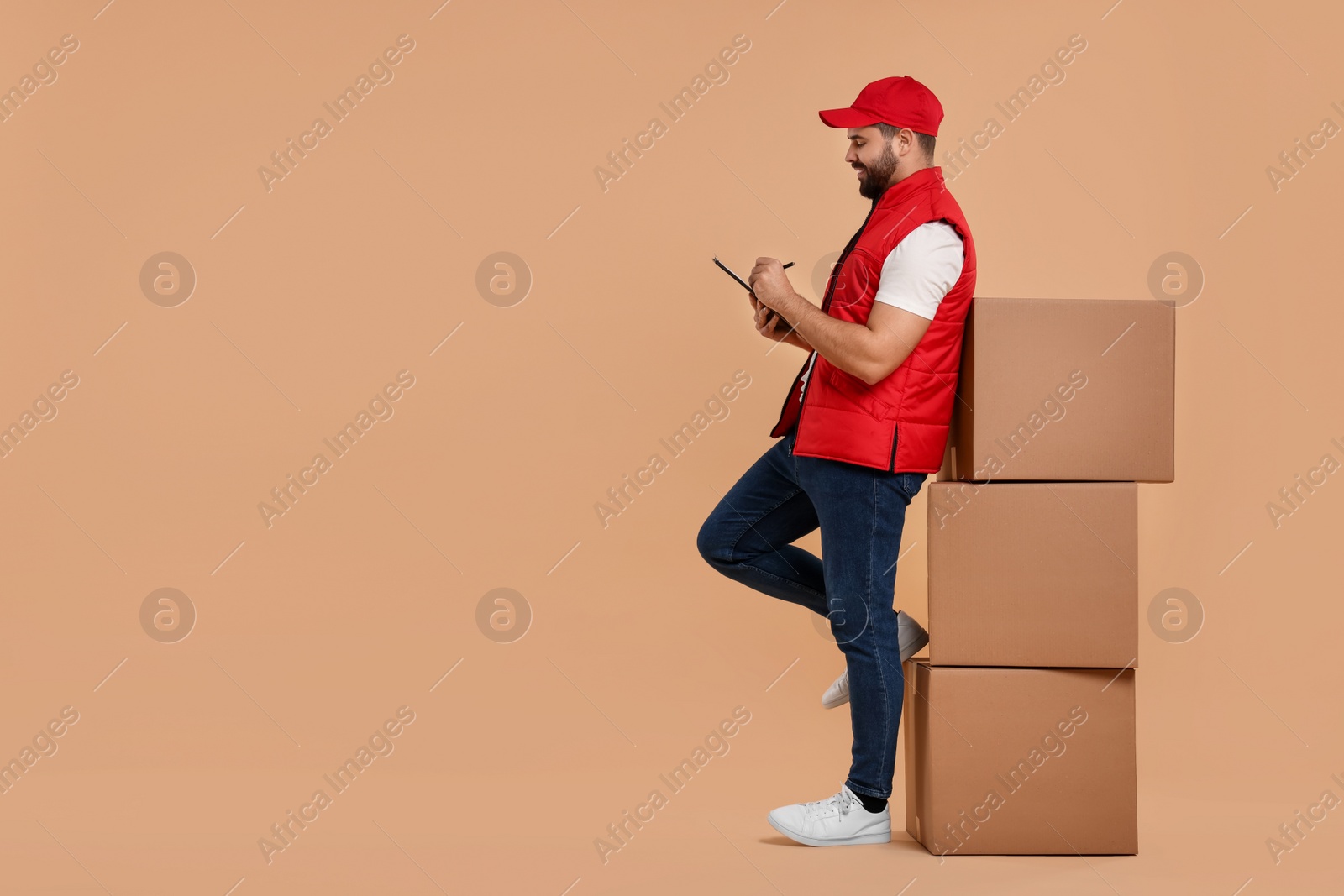 Photo of Courier with clipboard and stack of parcels on light brown background. Space for text