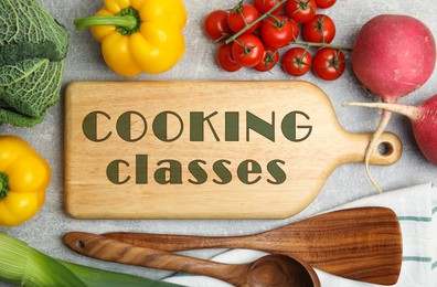 Image of Wooden board with inscription Cooking Classes and different fresh vegetables on light grey table, flat lay