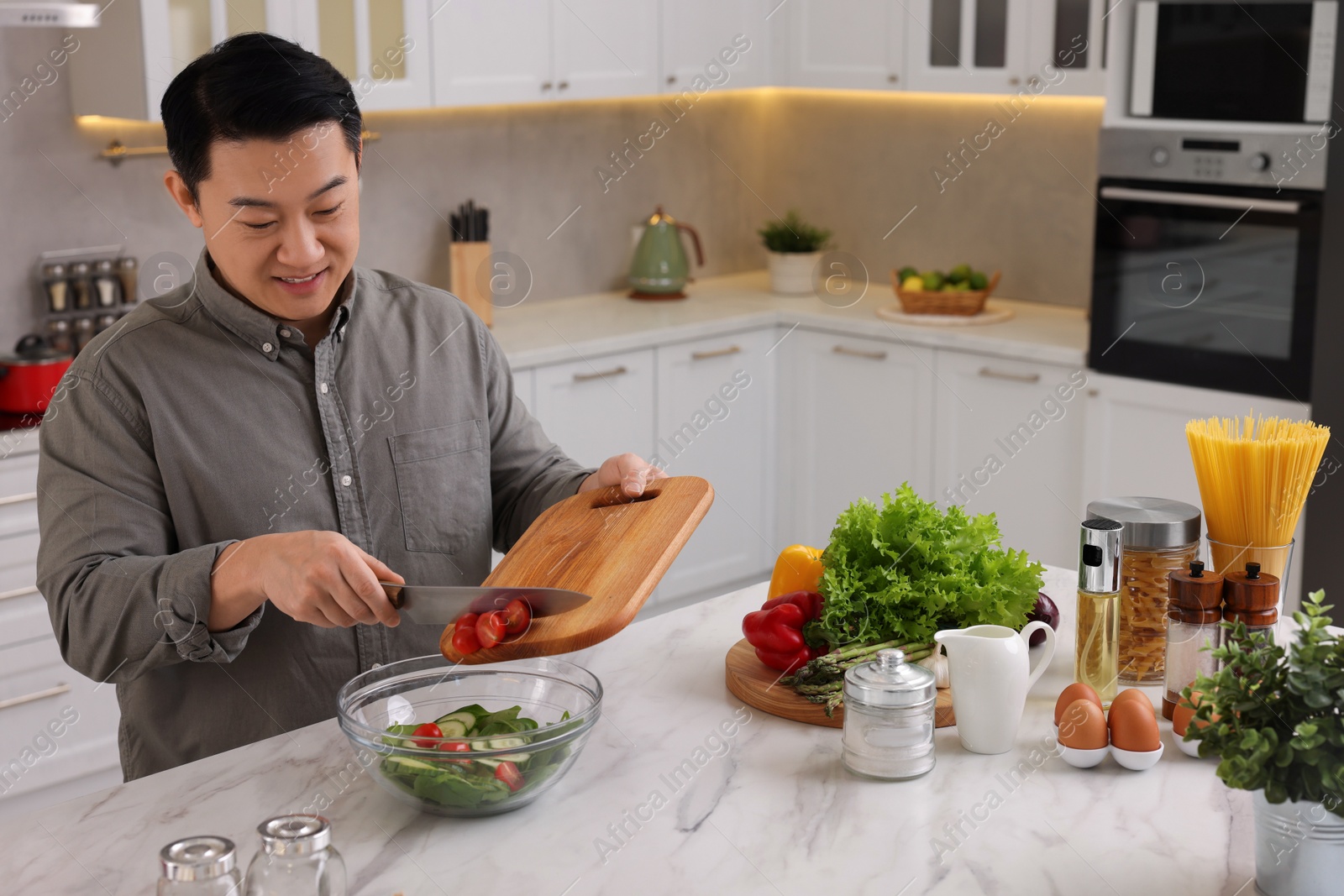 Photo of Cooking process. Man adding cut tomatoes into bowl at countertop in kitchen