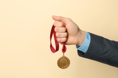 Photo of Man holding golden medal on color background, closeup. Space for text