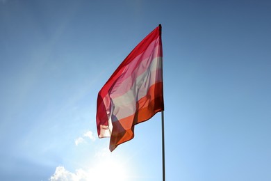 Bright lesbian flag fluttering against blue sky, space for text