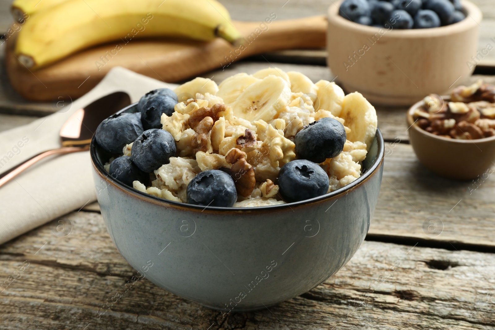 Photo of Tasty oatmeal with banana, blueberries and walnuts served in bowl on wooden table