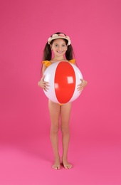 Cute little child in beachwear with bright inflatable ball on pink background