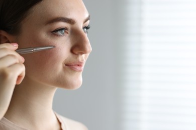 Photo of Beautiful woman drawing freckles with pen indoors. Space for text