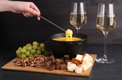 Woman dipping piece of bread into fondue pot with melted cheese at black wooden table, closeup