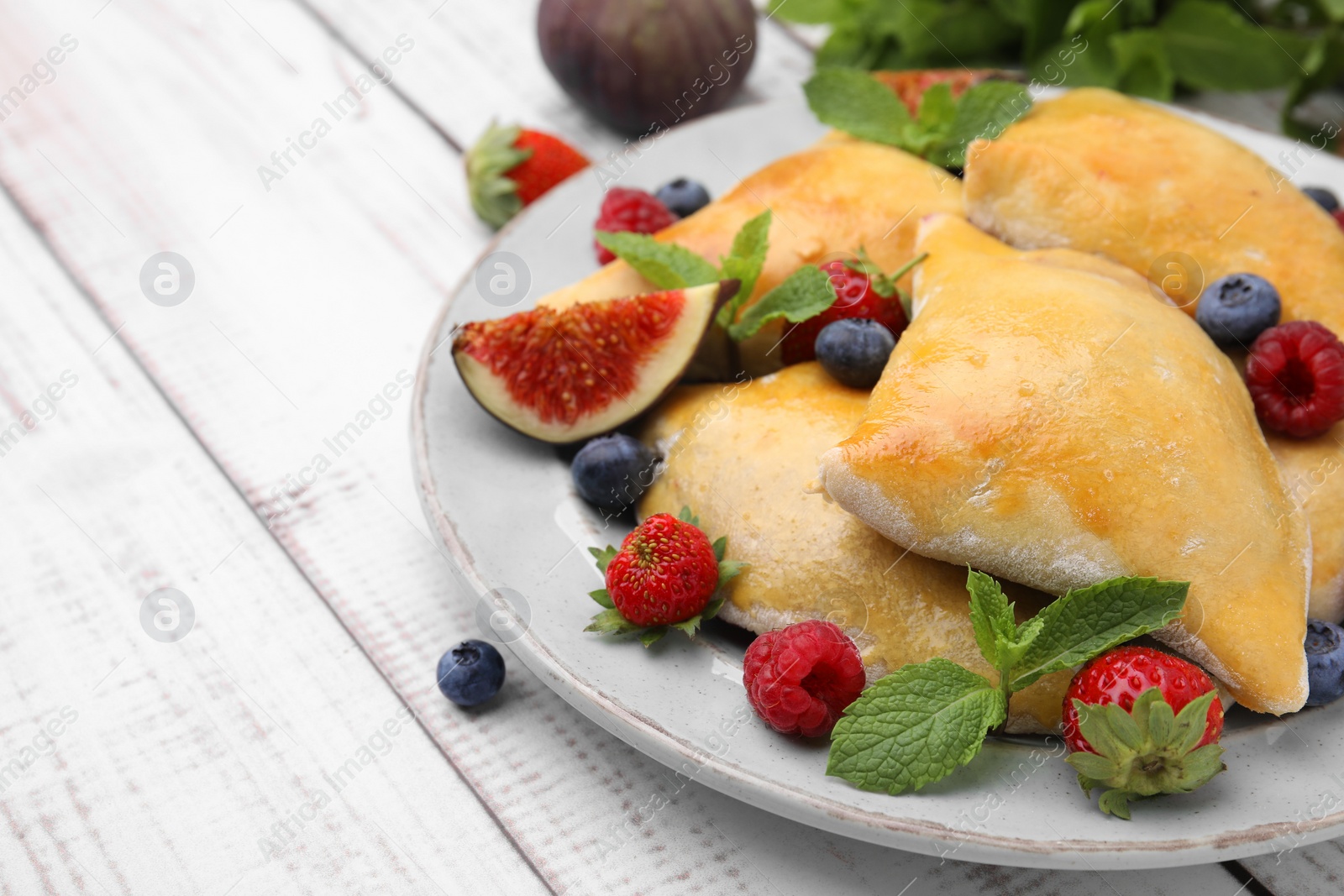 Photo of Delicious samosas with figs and berries on white wooden table, closeup