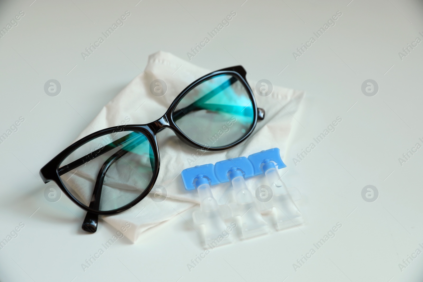 Photo of Single dose eye drops, glasses and fabric on white table