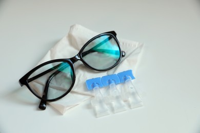 Photo of Single dose eye drops, glasses and fabric on white table