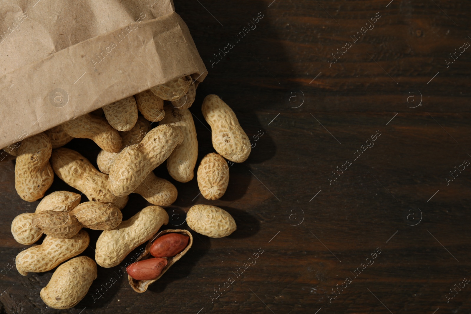 Photo of Paper bag with fresh unpeeled peanuts on wooden table, top view. Space for text