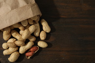 Photo of Paper bag with fresh unpeeled peanuts on wooden table, top view. Space for text