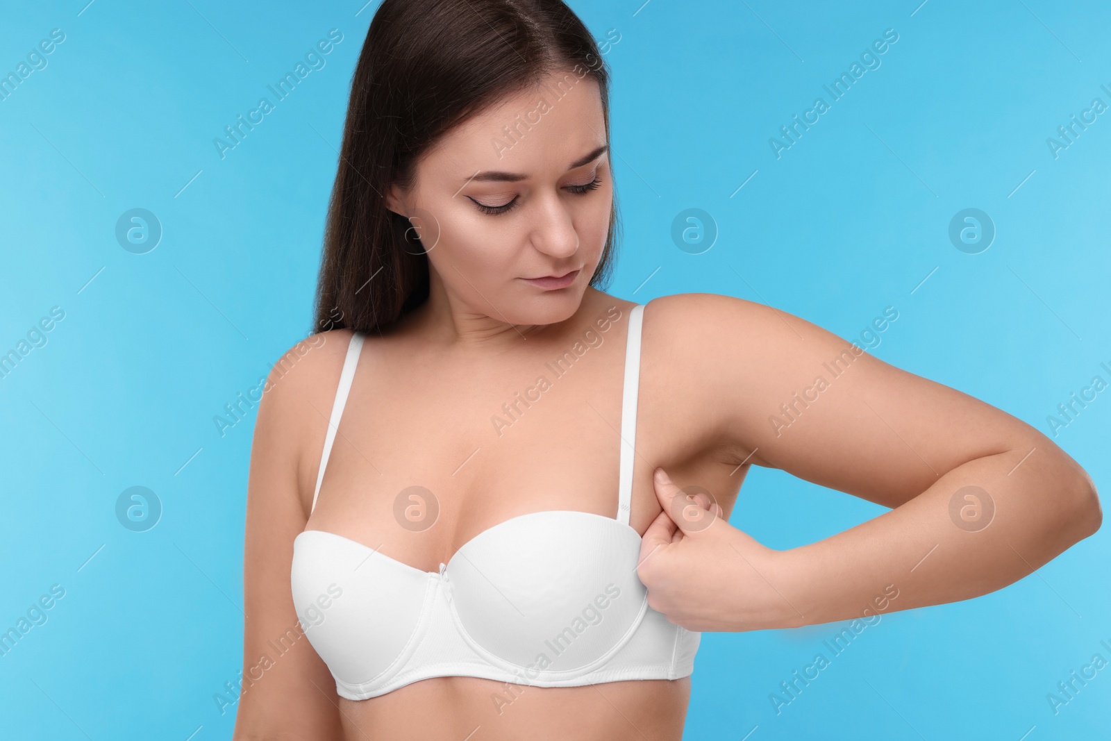 Photo of Mammology. Woman in bra doing breast self-examination on light blue background