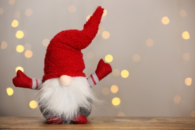 Photo of Cute Christmas gnome on wooden table against blurred festive lights. Space for text