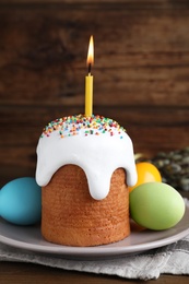 Photo of Traditional Easter cake with burning candle and colorful eggs on wooden table