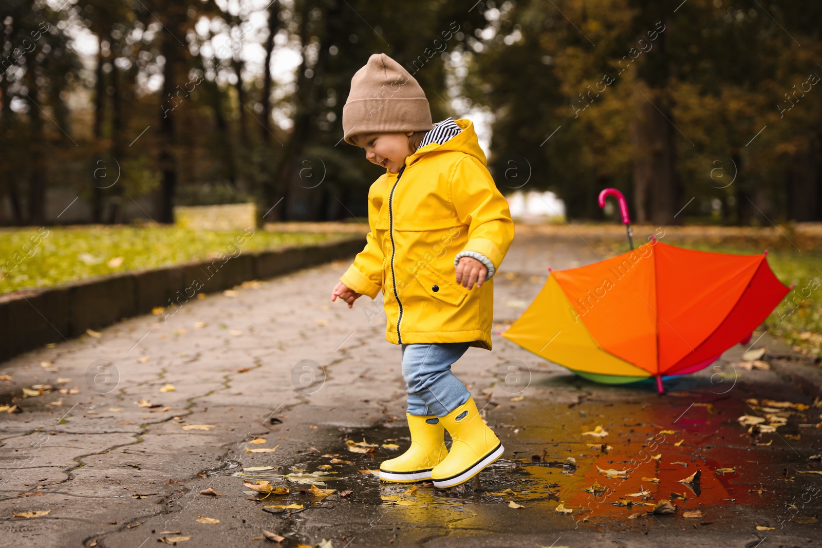 Photo of Cute little girl walking in puddle near colorful umbrella outdoors