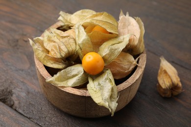 Photo of Ripe physalis fruits with calyxes in bowl on wooden table, closeup