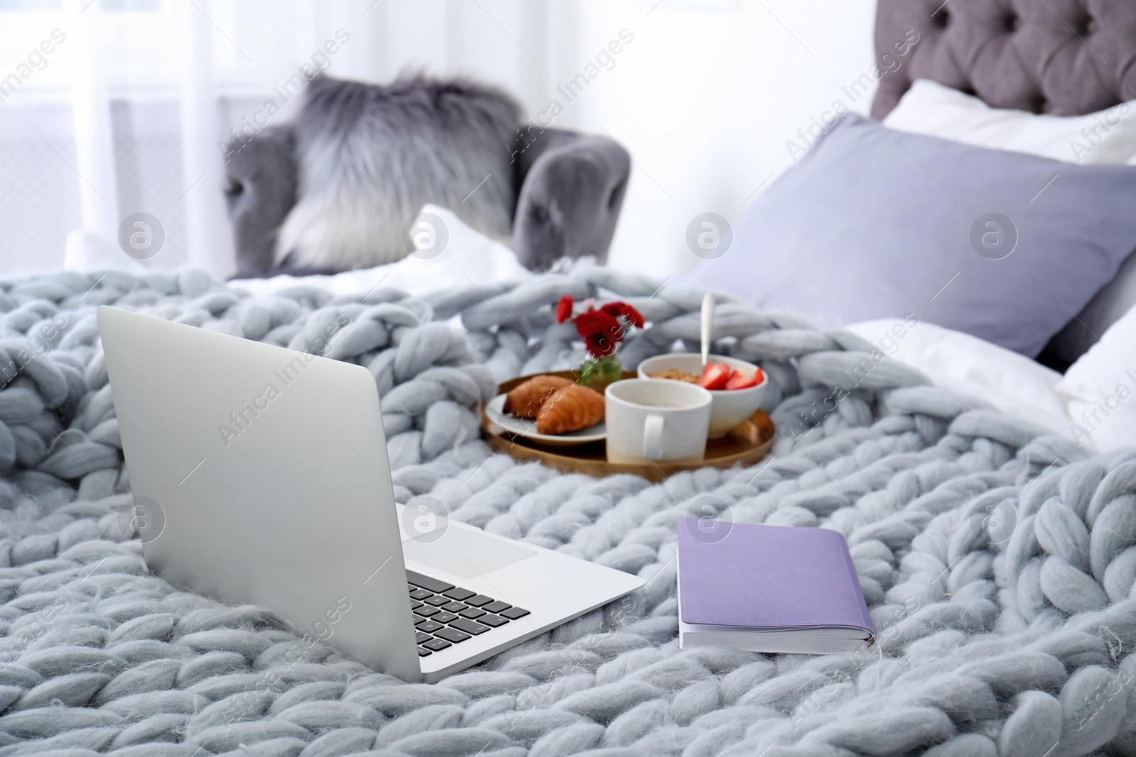 Photo of Laptop, notebook and tray with breakfast on bed in stylish room interior