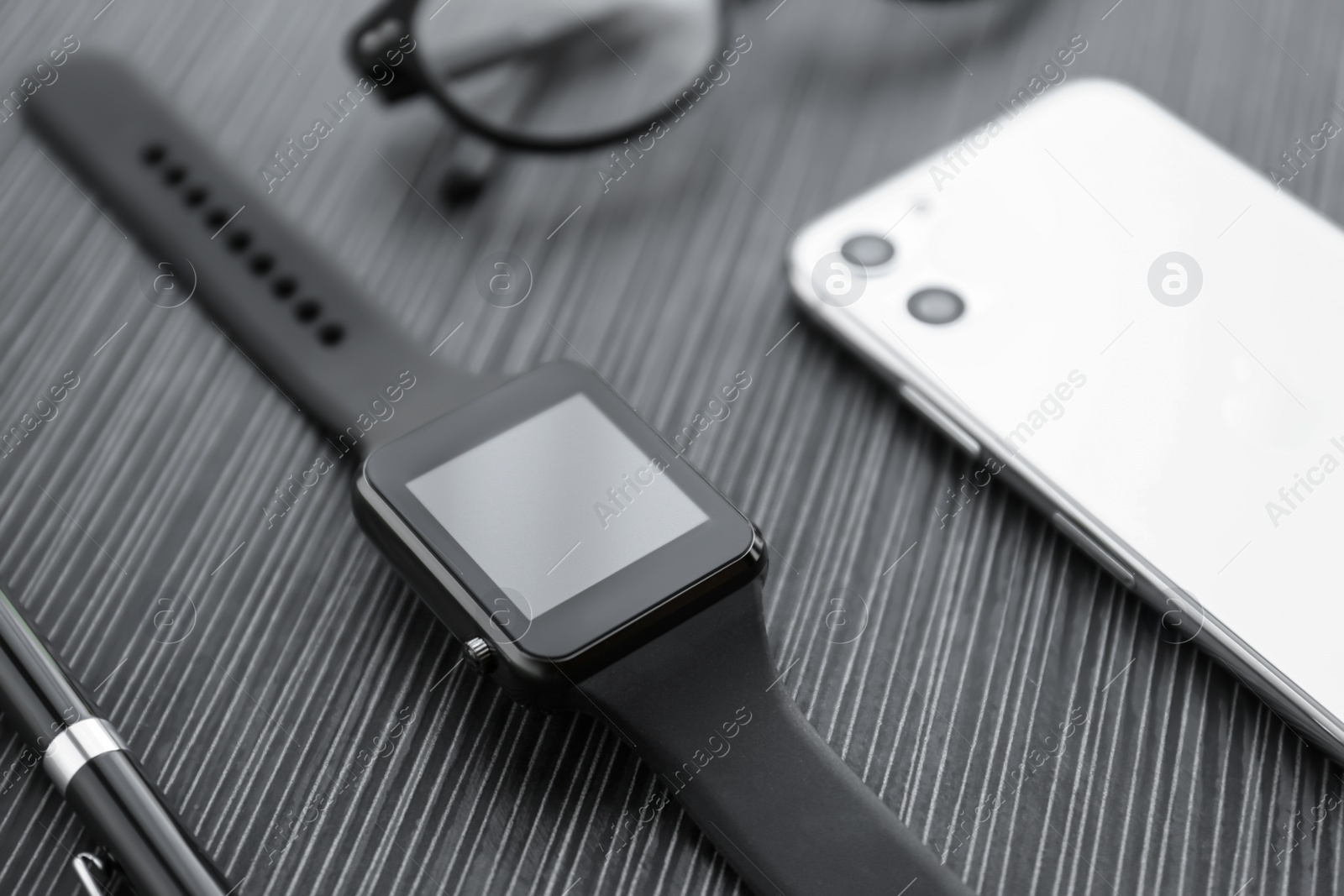 Stylish smart watch, phone and pen on black table, closeup Photo of Stylish smart watch, phone and pen on black table, closeup