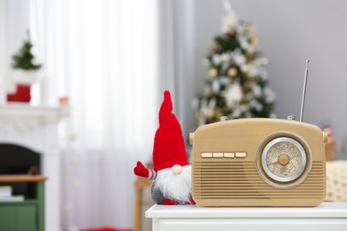 Stylish radio and Christmas gnome on white table in decorated room. Space for text