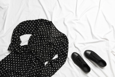 Photo of Stylish black dress and shoes on white fabric, flat lay