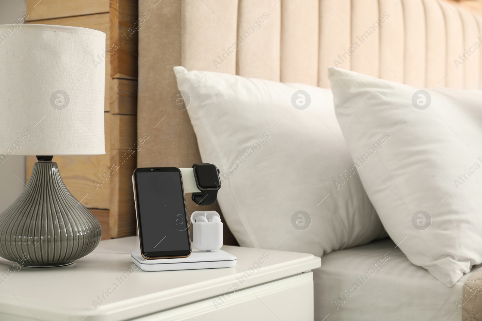 Photo of Different gadgets charging on wireless pad in bedroom