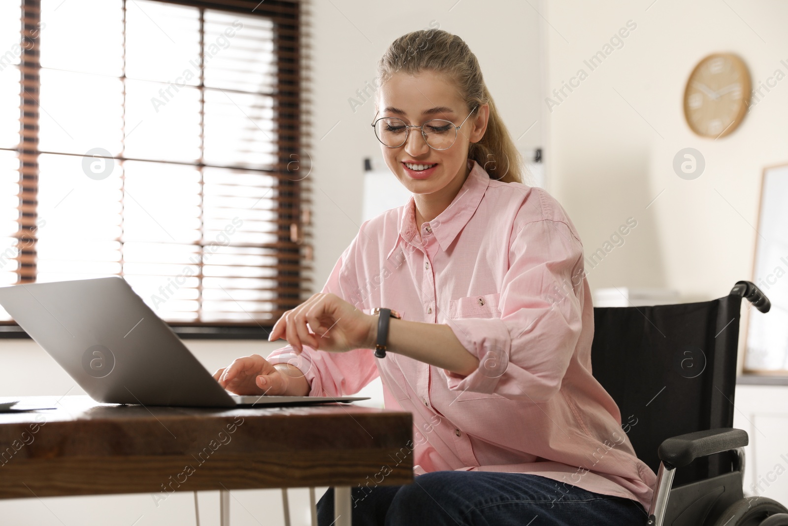 Photo of Portrait of woman in wheelchair with laptop at table indoors