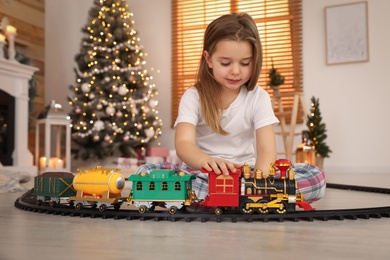 Photo of Little girl playing with colorful train toy in room decorated for Christmas
