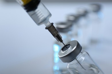 Photo of Filling syringe with medicine from vial on blurred background, closeup