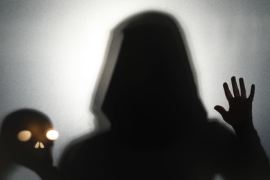 Photo of Silhouette of ghost and skull behind glass against light grey background