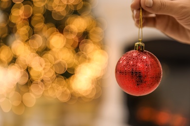 Photo of Woman holding beautiful holiday ornament against blurred Christmas lights, closeup