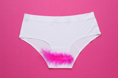 Woman's panties with feather on pink background, top view. Menstrual cycle