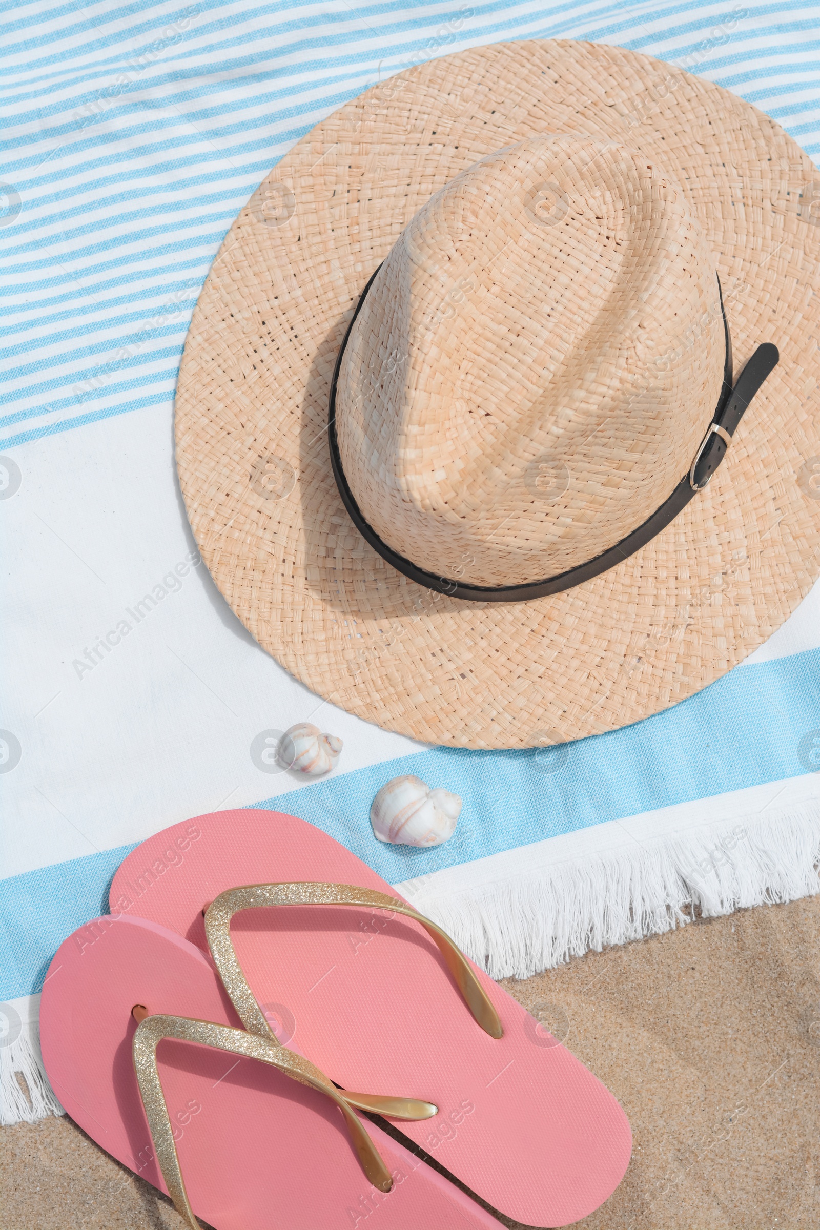 Photo of Beach towel with straw hat, seashells and flip flops on sand, flat lay