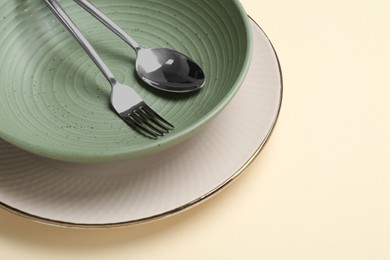 Stylish ceramic plate, bowl and cutlery on beige background, closeup