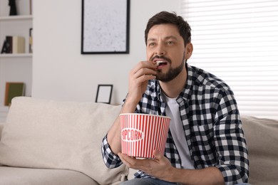 Photo of Man watching TV while eating popcorn on sofa at home