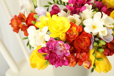 Photo of Vase with bouquet of spring freesia flowers on chair, closeup