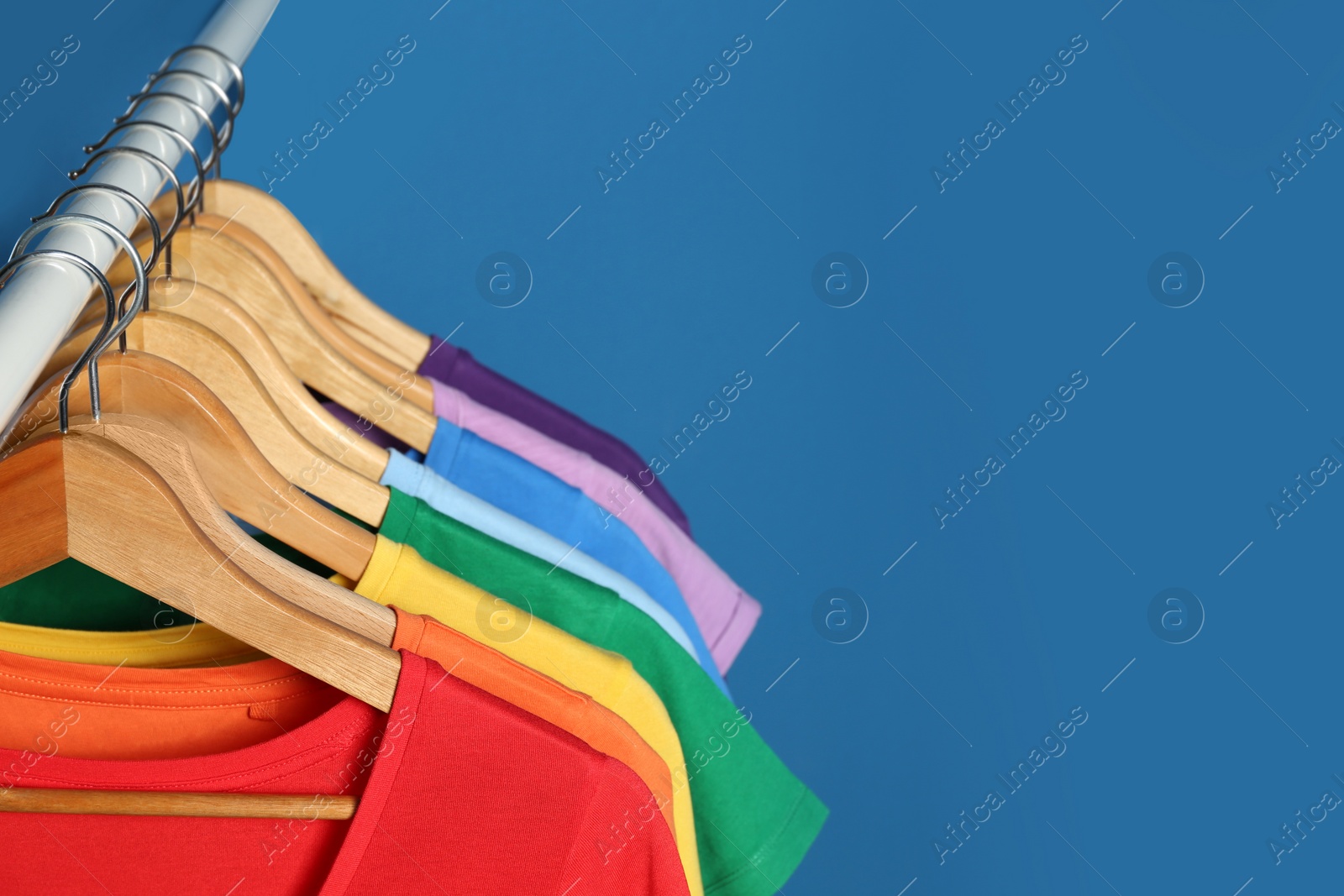 Photo of Bright clothes on blue background, space for text. Rainbow colors