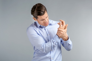 Photo of Young man suffering from pain in wrist on grey background