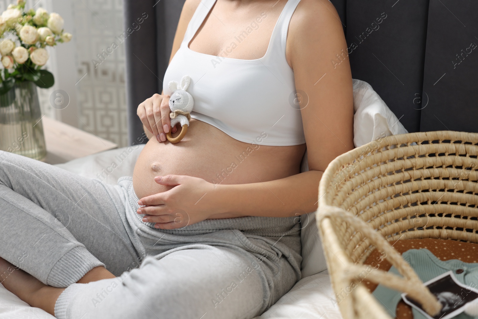 Photo of Pregnant woman with bunny toy sitting on bed indoors, closeup